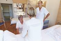 Zwei Gesundheits- und Krankenpflegerinnen im Gespräch mit einer Patientin am Krankenbett