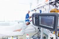 Patient im Bett auf der Intensivstation im Vordergrund ein Kontrollmonitor