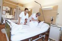 Zwei Gesundheits- und Krankenpflegerinnen mobiliseren eine Patientin im Bett